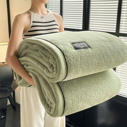 Person holding a green blanket with a brand label in a room with blinds.