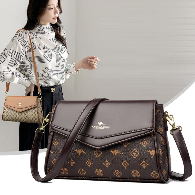 Brown patterned handbag with a visible brand logo, held by a person against a neutral background.
