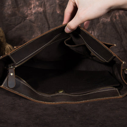 Hand holding open an empty dark brown leather bag against a dark background
