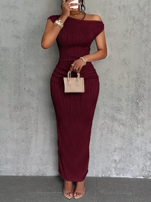Woman wearing a burgundy off-shoulder dress against a gray concrete wall.