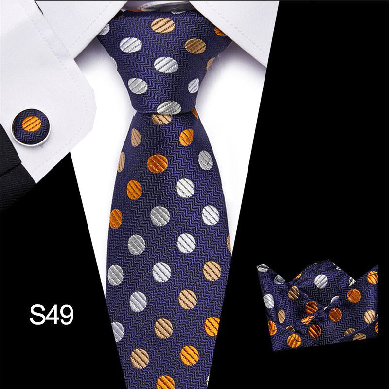 Navy blue tie with orange and gray polka dots, matching pocket square, and cufflinks on a white shirt.