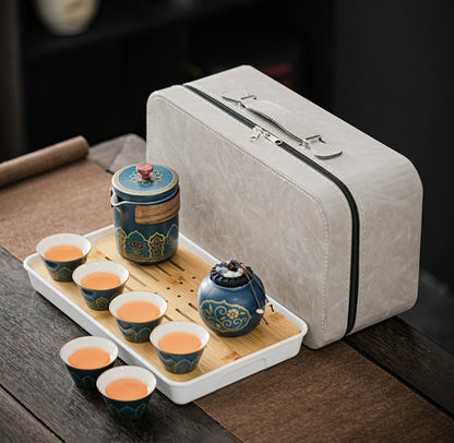 Tea set with blue ceramic teapot and cups on a wooden tray next to a gray carrying case.