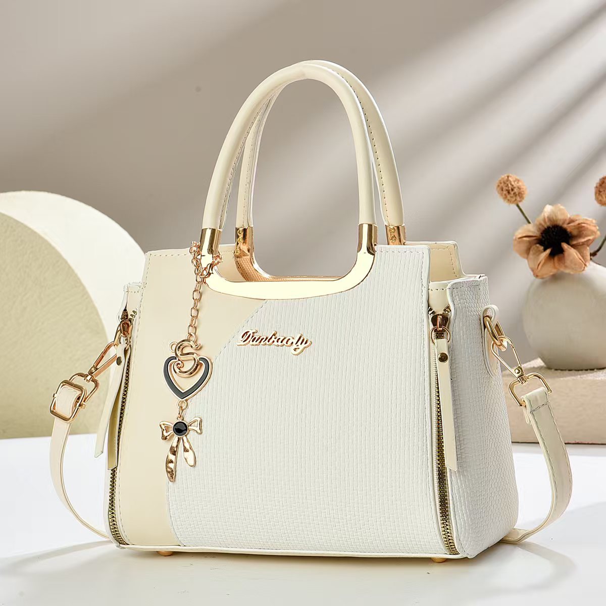 White small square crossbody bag with top handles and gold zipper, heart and bow charm