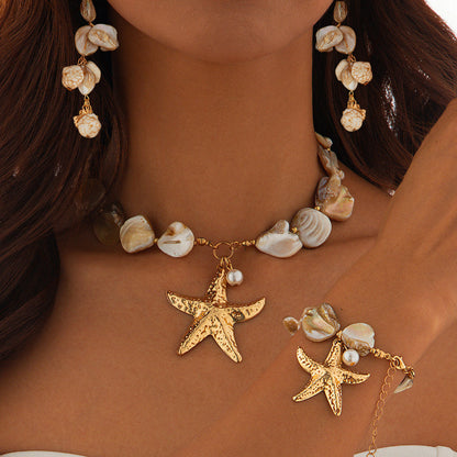 Women's Necklace and bracelet with starfish and shell charms on a person wearing a brown top.