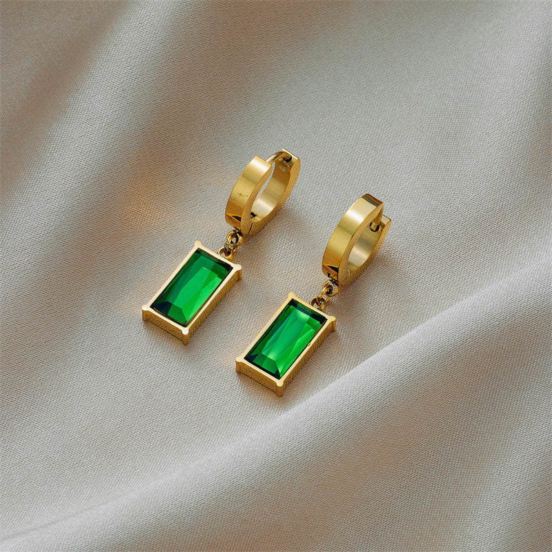 Gold hoop earrings with green gemstones on a beige fabric background