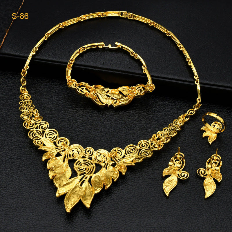 Gold-plated necklace, bracelet, and dangling earrings set arranged on a dark base