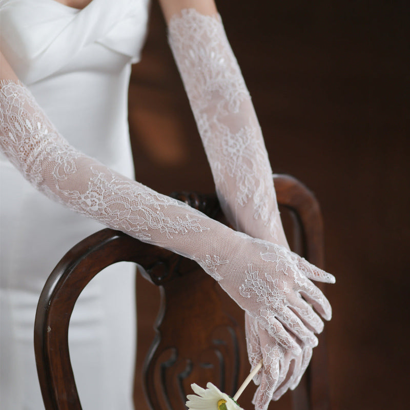 Close-up of lace gloves worn by a person sitting on a wooden chair.