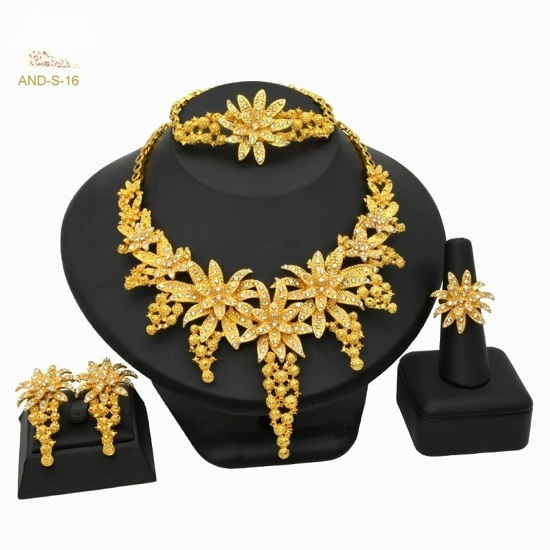 Gold jewelry set including necklace, bracelet, earrings, and ring on a black stand with 'AND-S-16' branding.
