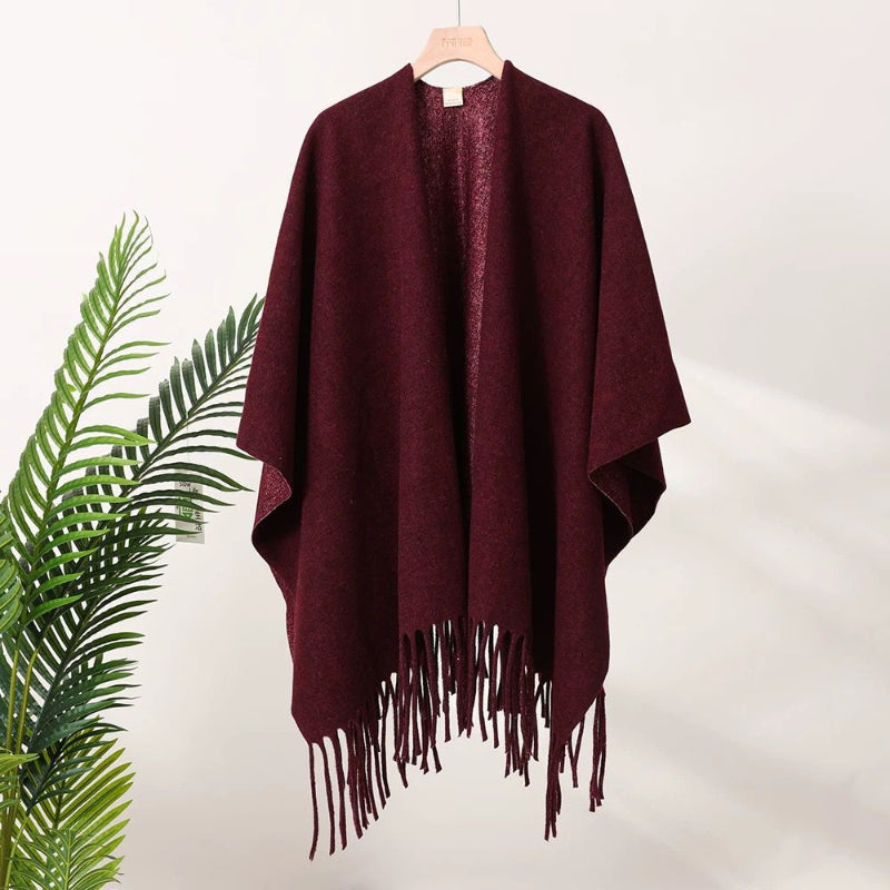 Burgundy poncho with fringe on a hanger against a white background
