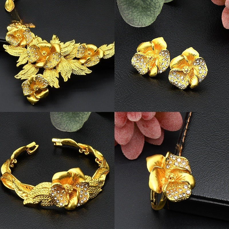 Set of gold floral jewelry including necklace, earrings, bracelet, and hairpin on a dark surface with pink flowers.