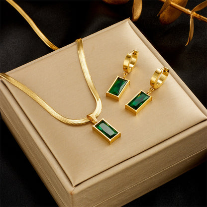 Gold necklace and earrings with green gemstones on a beige jewelry box.