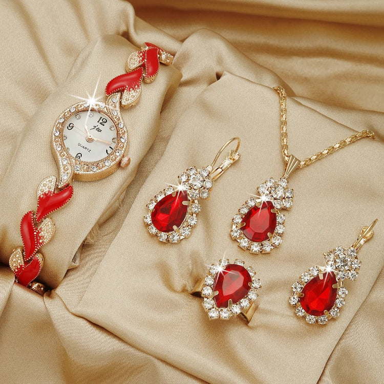 Jewelry set with red gemstones including a watch, necklace, and earrings on a beige fabric background.