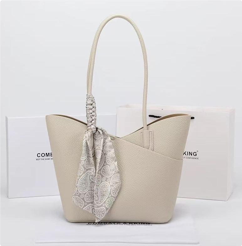 Beige handbag with a patterned scarf draped over it on a white background