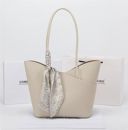 Beige handbag with a patterned scarf draped over it on a white background