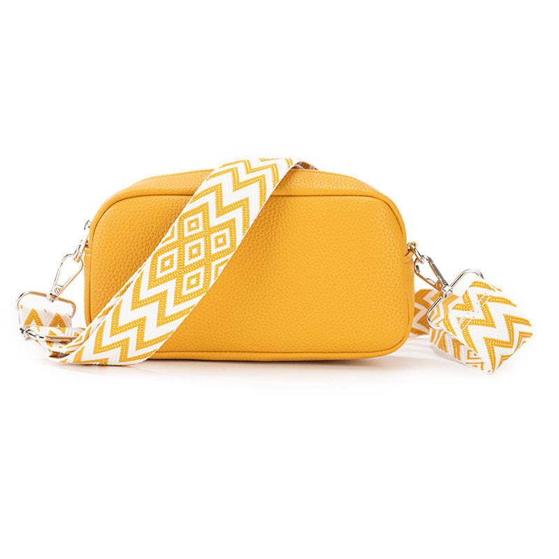 Yellow crossbody bag with a white and gold zigzag strap on a white background
