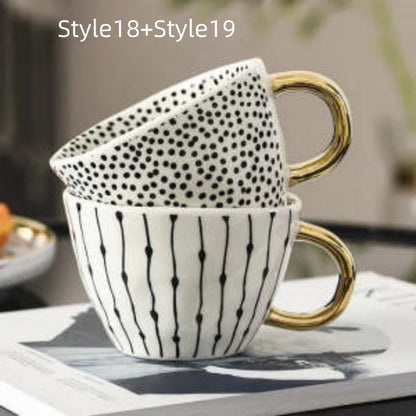 Two ceramic mugs with gold handles stacked on a surface, featuring black dot patterns.