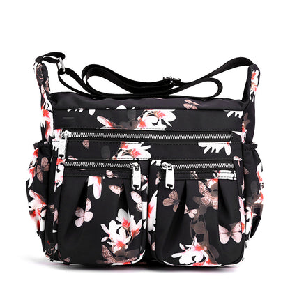 Large-capacity crossbody bag in black with white floral print and several zip front pockets.