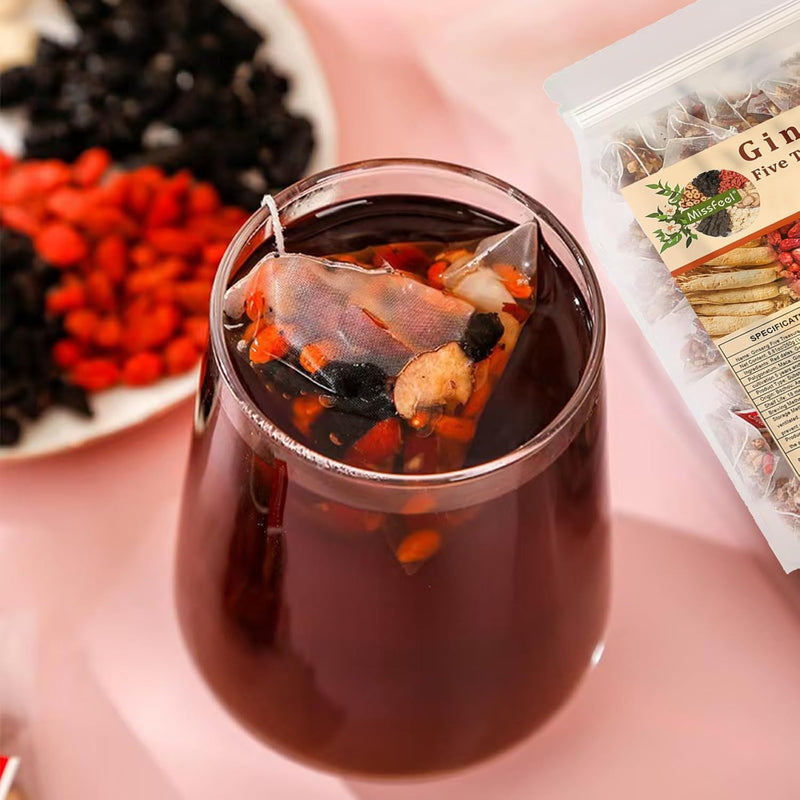 Glass cup of dark herbal tea with steeped ingredients and a tea pouch beside it