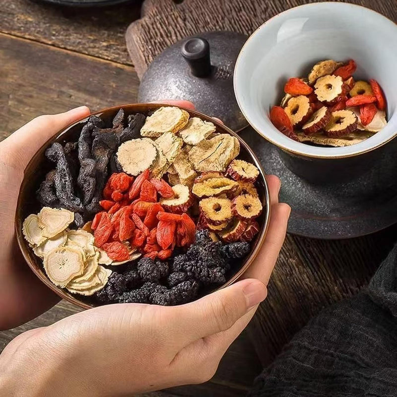 Hand holding a bowl of mixed dried herbal tea ingredients with red berries and pale roots